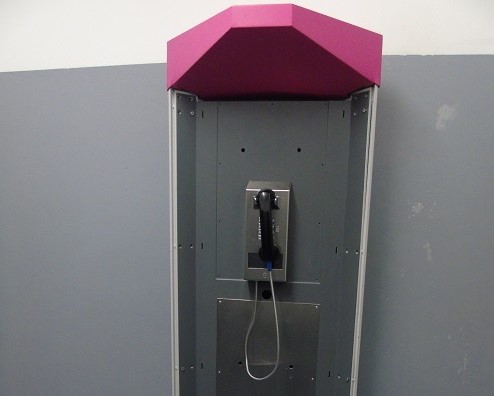 Ein Telefon hängt an der Wand, dahinter ist ein Gang innerhalb einer Justizvollzugsanstalt zu sehen.